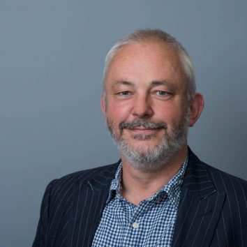 Photography of Jerry Smith OBE. He is a white man with short grey hair smiling at the camera.